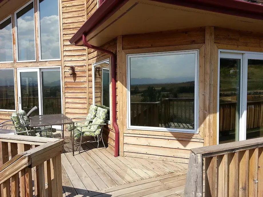 Wooden cabin deck with outdoor seating and large windows overlooking a scenic landscape