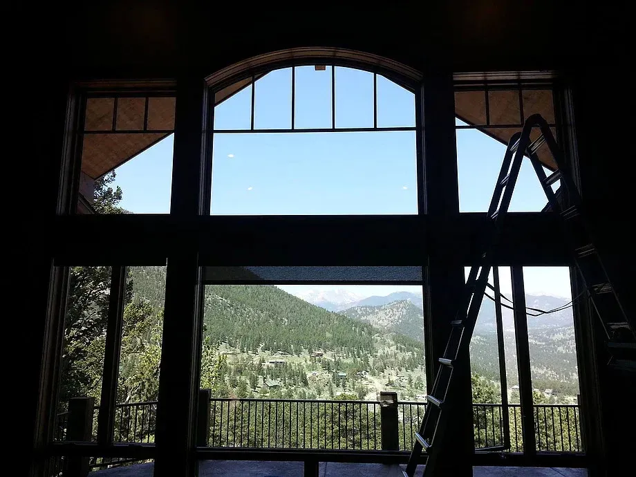 Mountain view through large arched window with a ladder on the right, inside a dark room