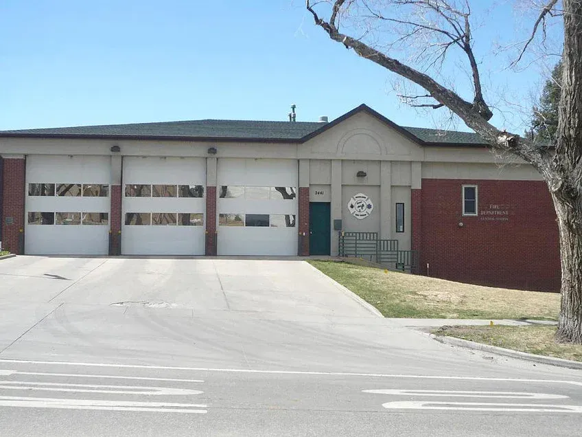 Small brick fire station with three garage bays and an American flag on the front lawn