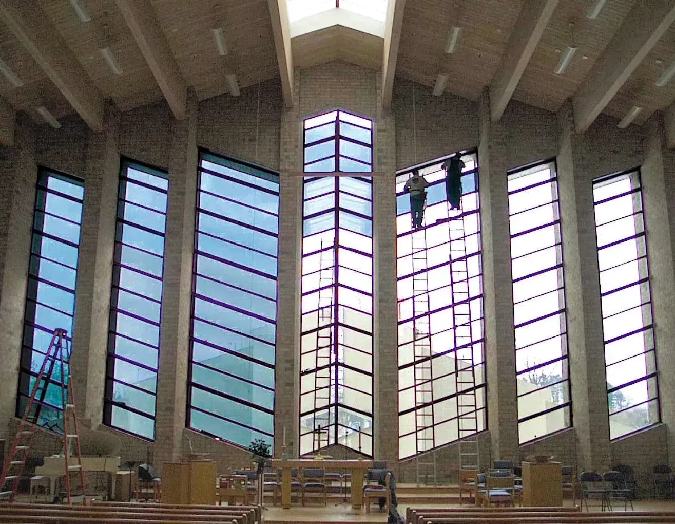 Interior of a modern church sanctuary with tall stained-glass windows and a large cross-shaped central window