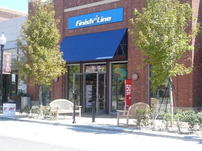 Storefront with blue awning and glass entrance at Finish Line, flanked by trees and outdoor benches