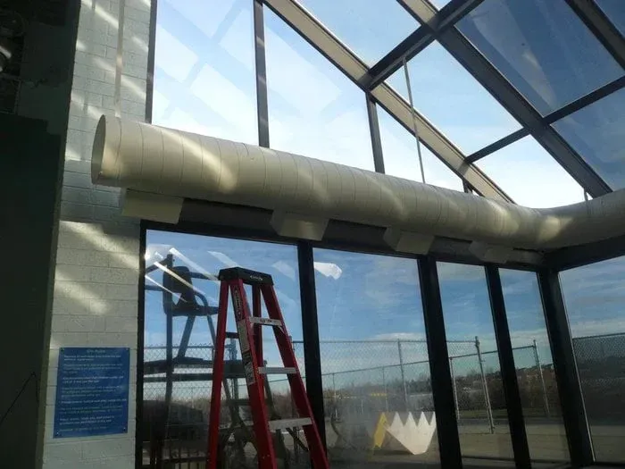 Red ladder in a glass atrium with a large white ventilation duct overhead.