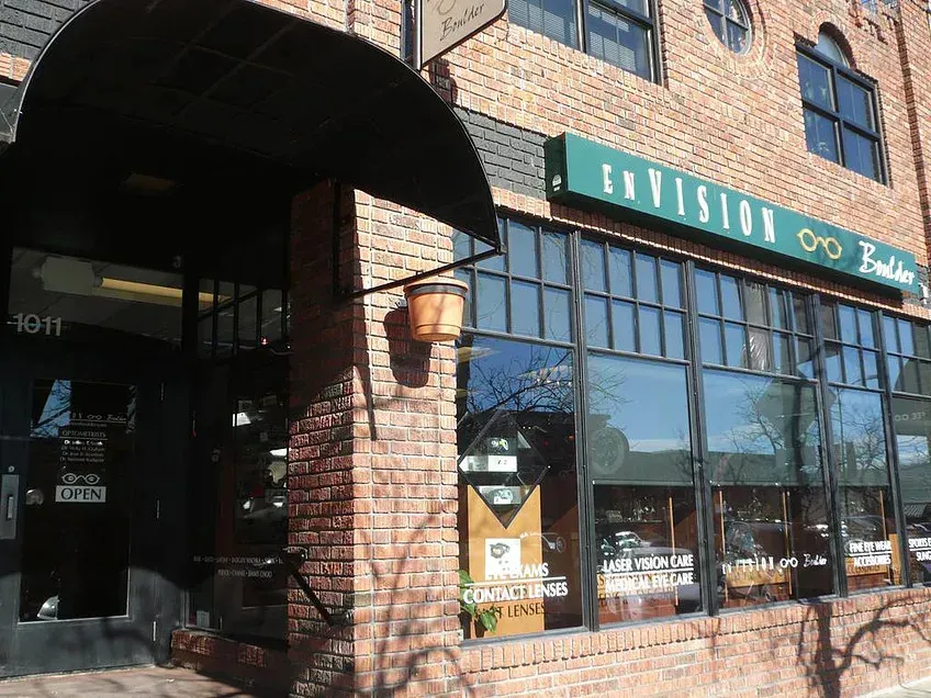 Brick storefront with teal sign and large windows on a sunny street corner.