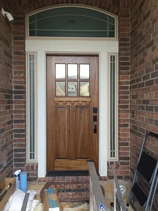 Front porch with a wooden front door, brick walls, and construction materials scattered on the steps.