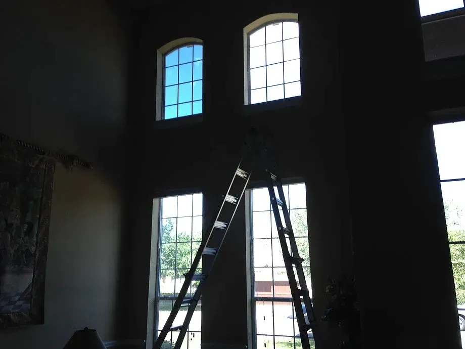 Ladder inside a dark room with tall arched windows and daylight outside