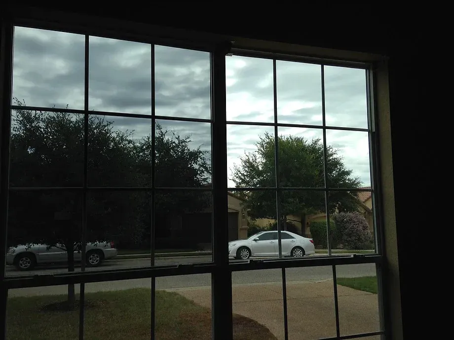 View through a window grid of a street with parked cars, trees, and cloudy sky