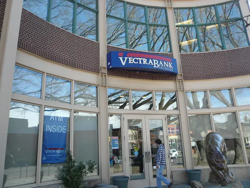 Entrance to Vectra Bank with blue signage and glass doors, plus a sculpture outside
