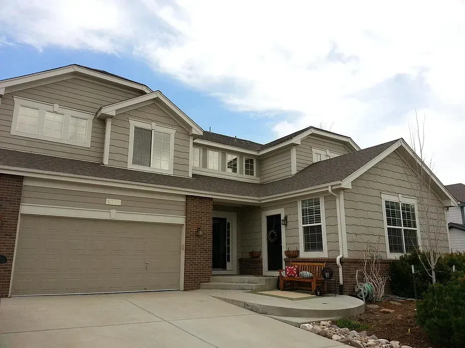 Two-story beige house with a large garage, front porch, and driveway under a cloudy sky