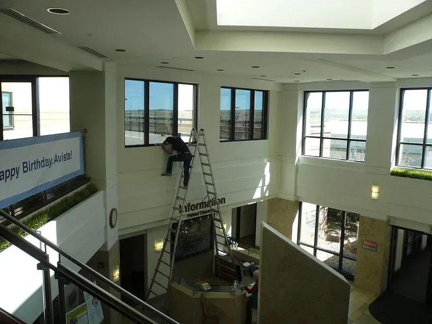 Atrium lobby with a ladder and worker cleaning windows under a bright skylight