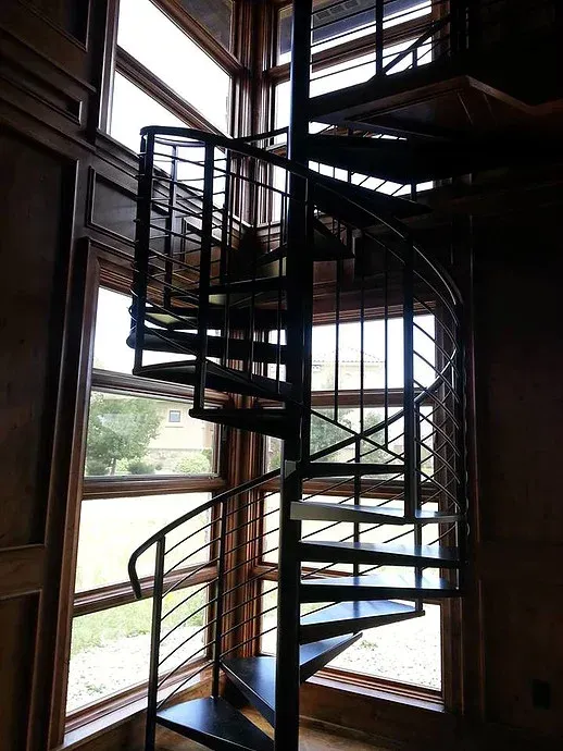 Spiral metal staircase inside a tall room with large windows and natural light