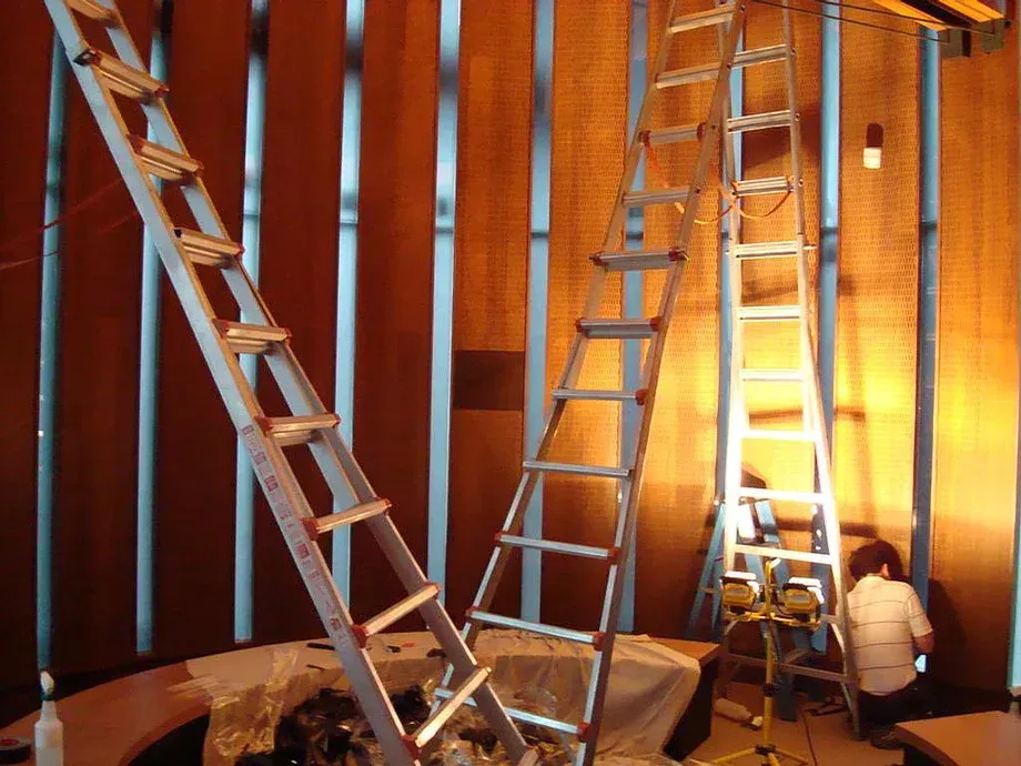 Ladders inside a wooden room with exposed framing; one person sits near the right wall.