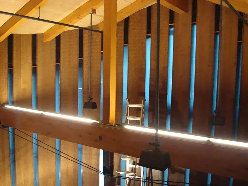 Wooden interior with vertical slats and blue-tinted window gaps, lit by a horizontal glowing light beam.
