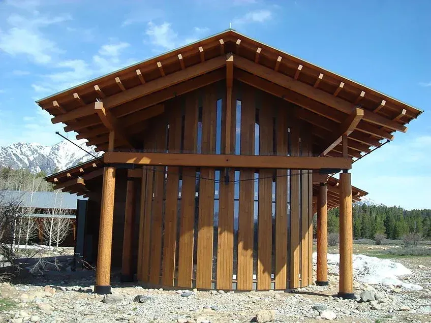 Small wooden cabin with a sloped roof and vertical slats in a rocky, open outdoor area