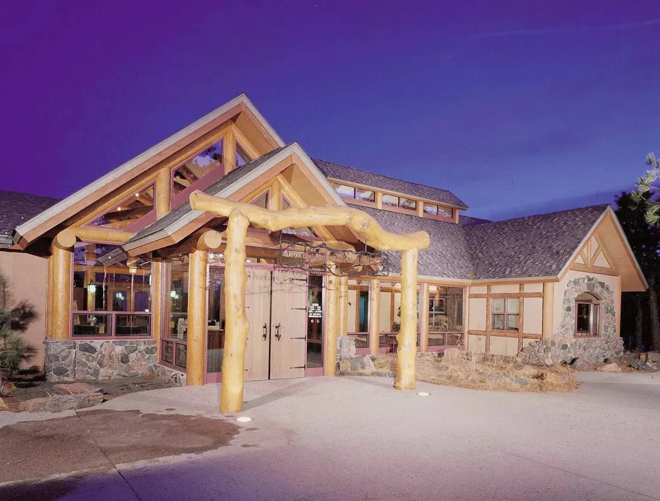 Wooden lodge entrance at dusk with lit timber beams and stone exterior
