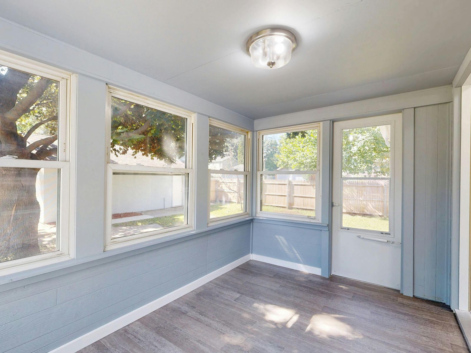 Bright sunroom with light blue walls, white trim, multiple windows, and a white door.
