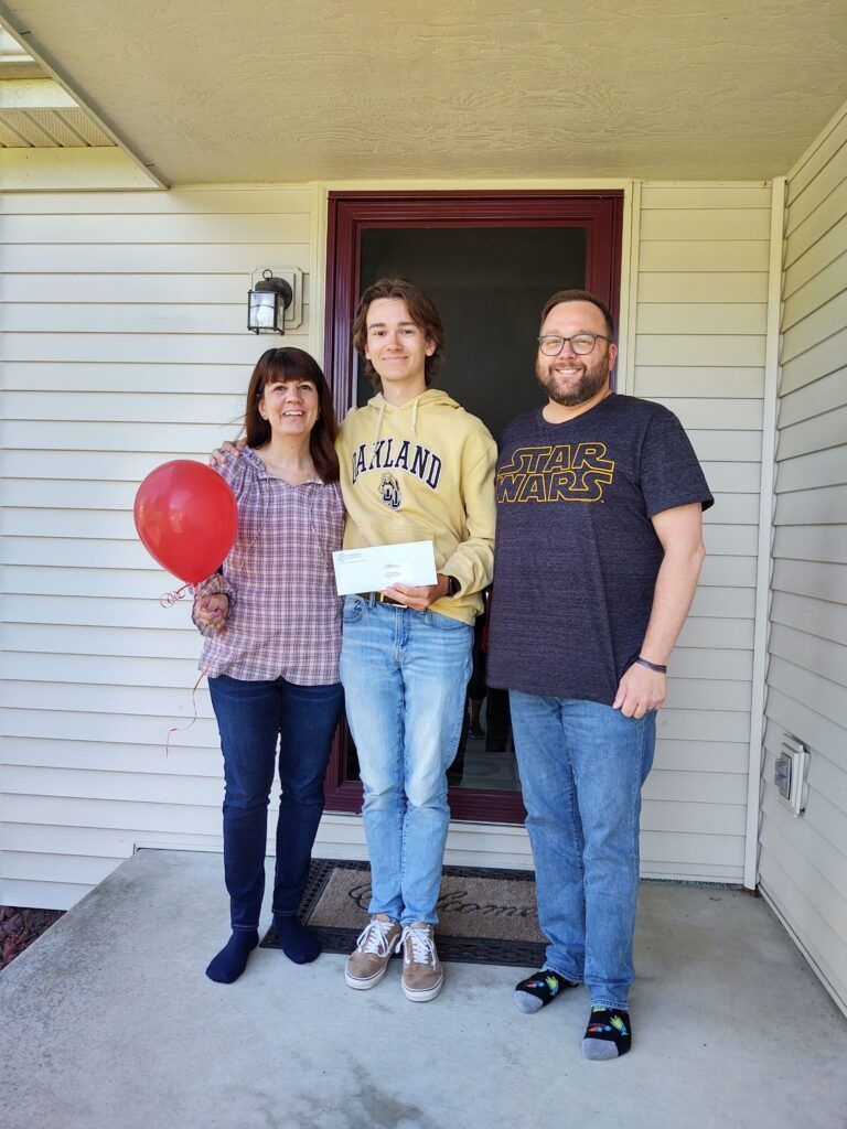 A man stands next to a woman holding a red balloon and a boy holding a check.
