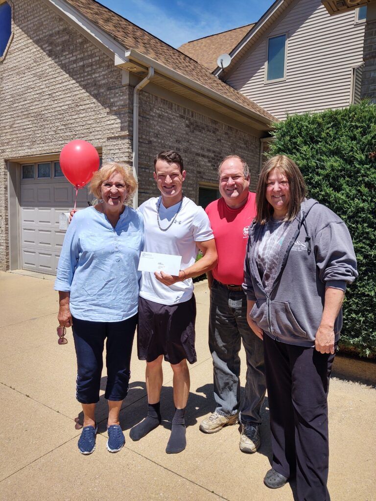 A group of people standing in front of a brick house with a check and a red balloon.