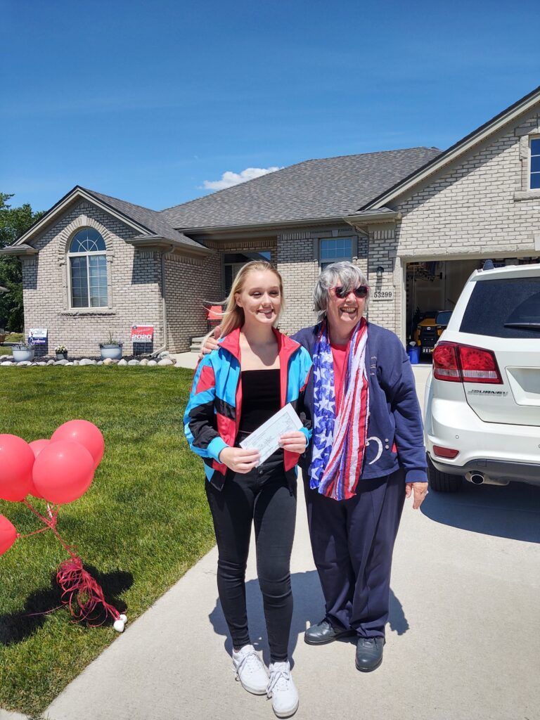 A woman holding a check standing next to an elder woman.