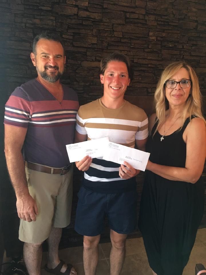 A man and a woman standing next to a young man holding a check.