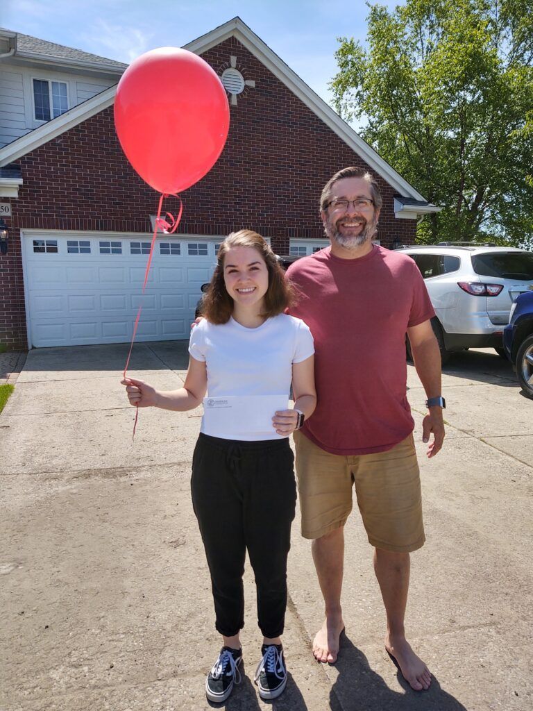 A woman holding a red balloon stands next to a man.