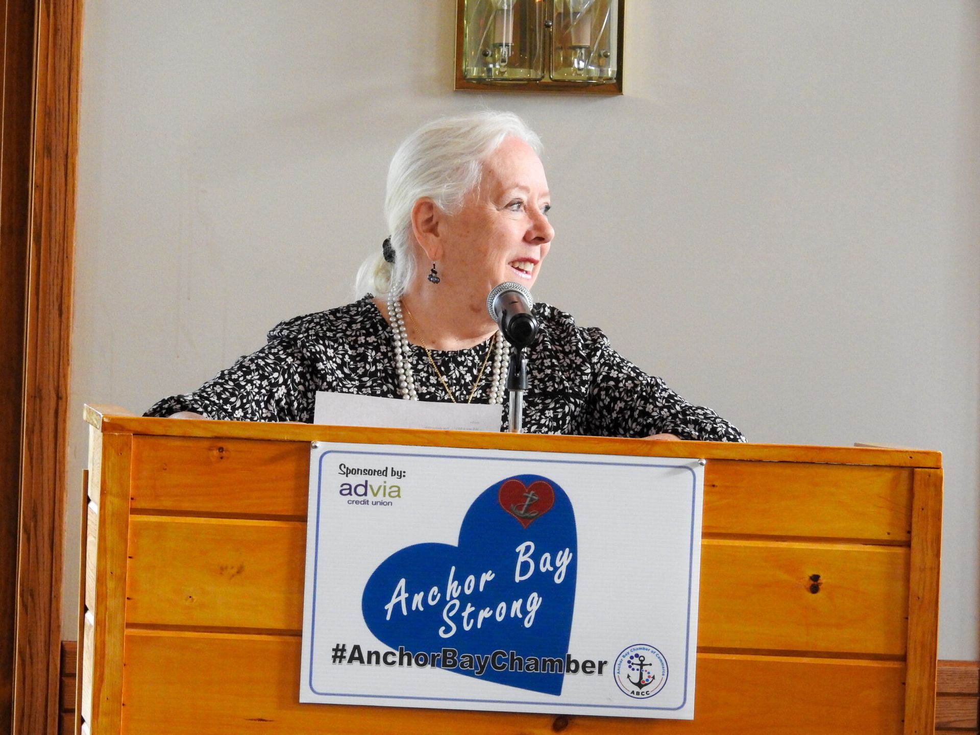 A woman stands at a podium with a sign that says Anchor Bay Strong.