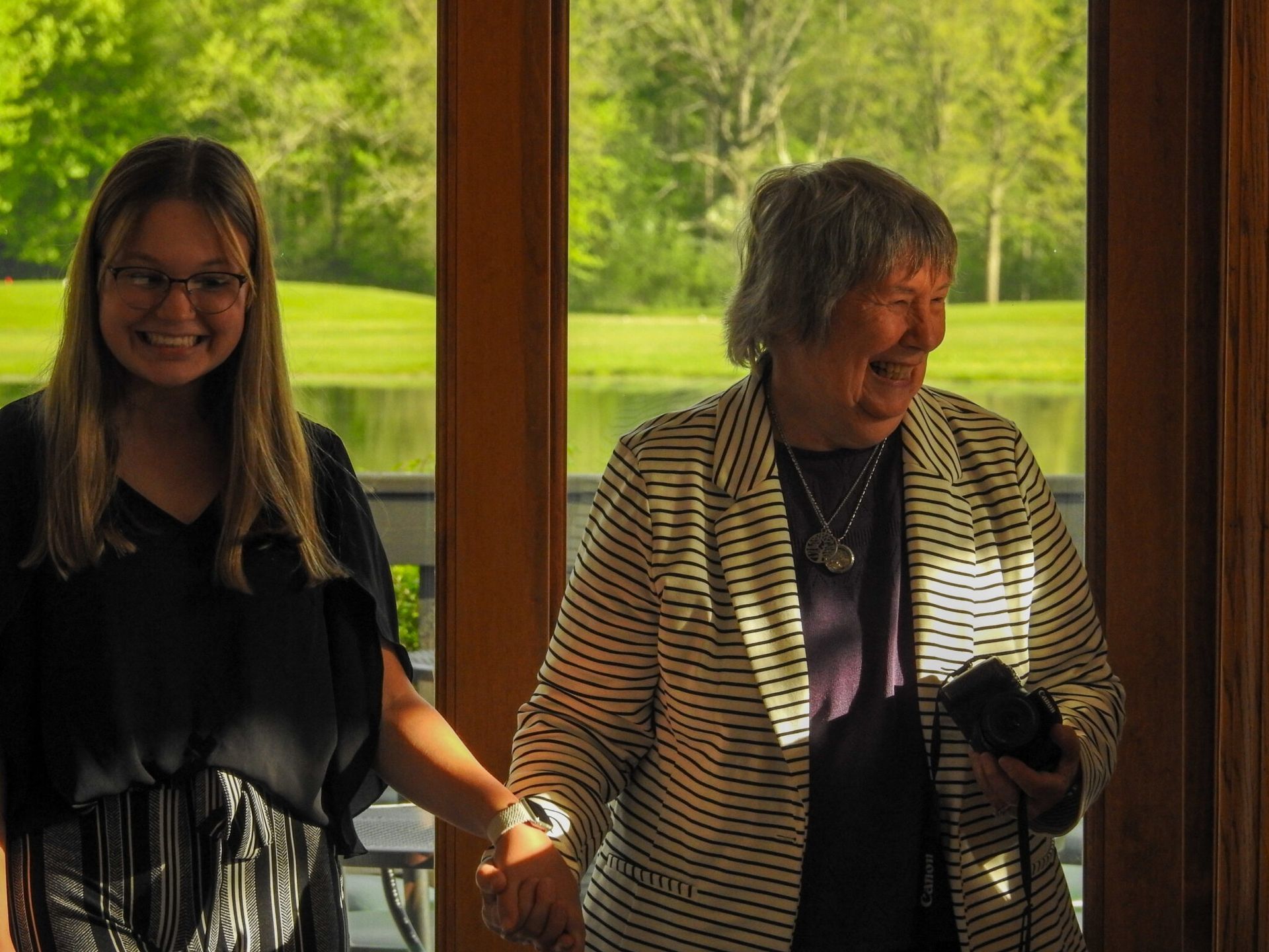 A woman in a striped jacket is holding a Canon camera.