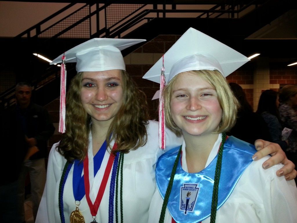 Two graduates in white gowns and caps.