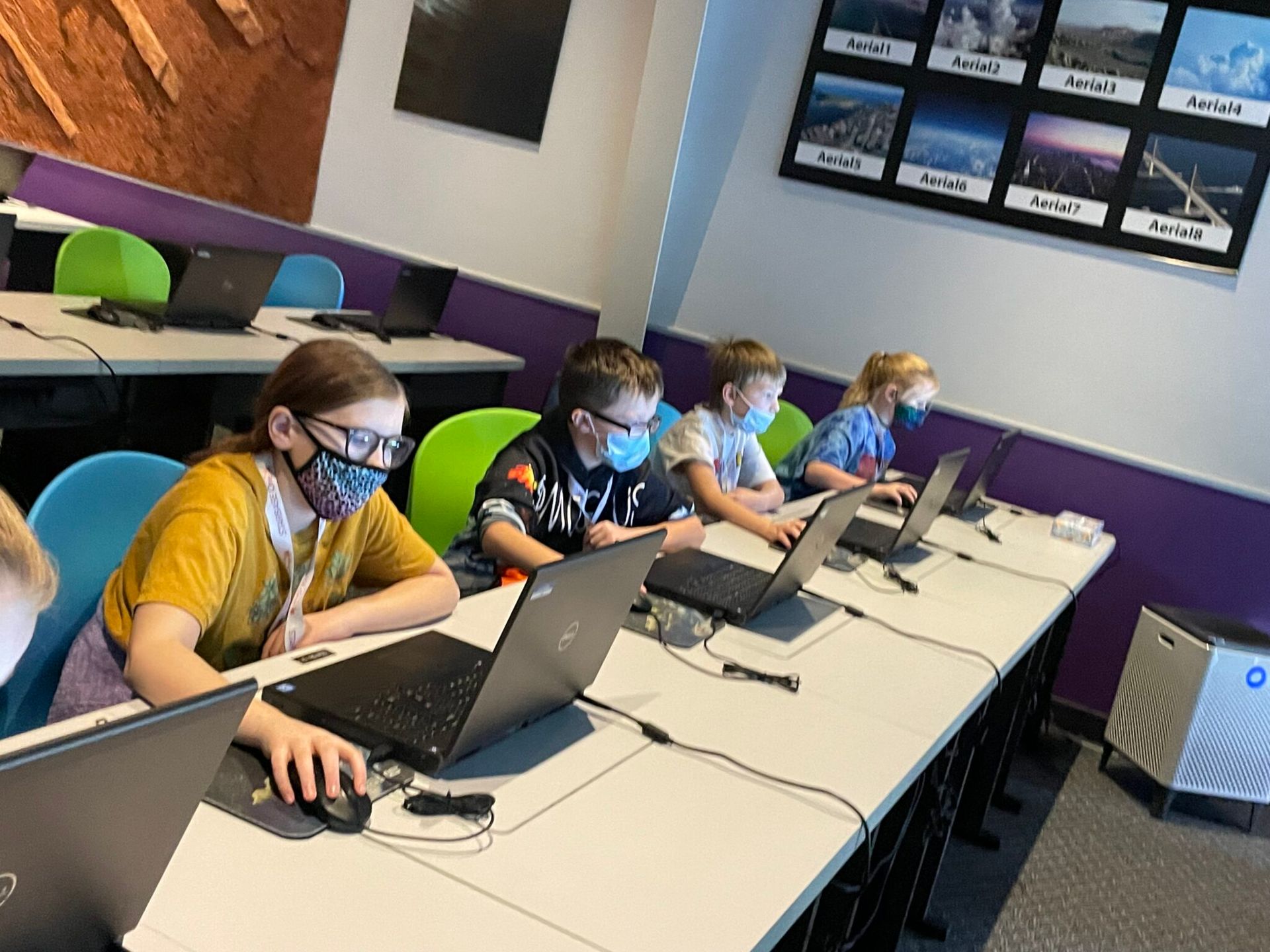 A group of children wearing face masks are using dell laptops.