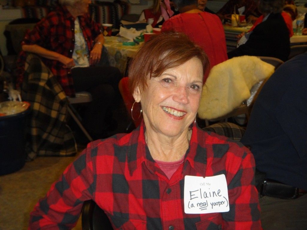 A woman wearing a plaid shirt has a name tag that says Elaine.