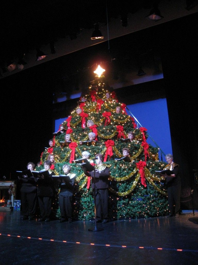 A group of people singing in front of a Christmas tree.