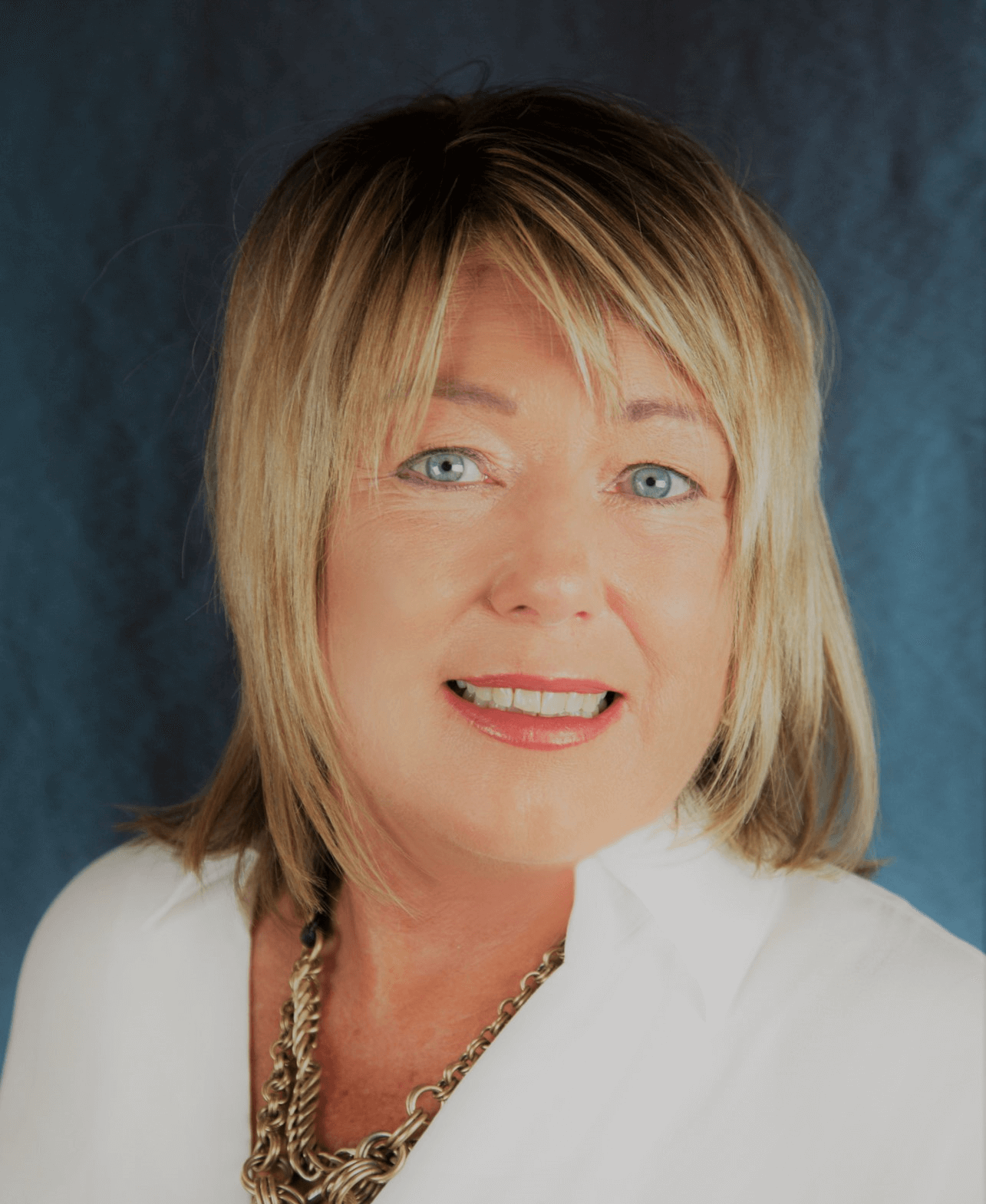 Woman with blonde hair, blue eyes, and white blazer smiling; dark blue background.