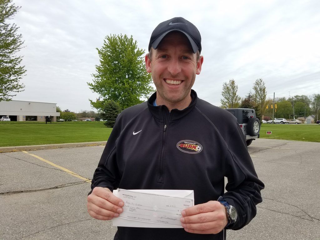 A man standing outside holding a check.