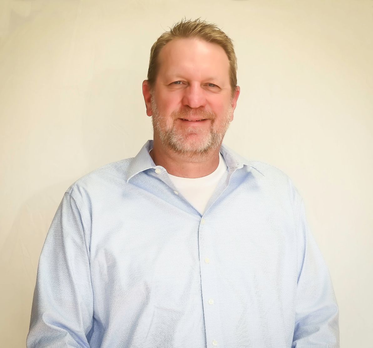 A man with a beard is wearing a blue shirt and smiling for the camera.