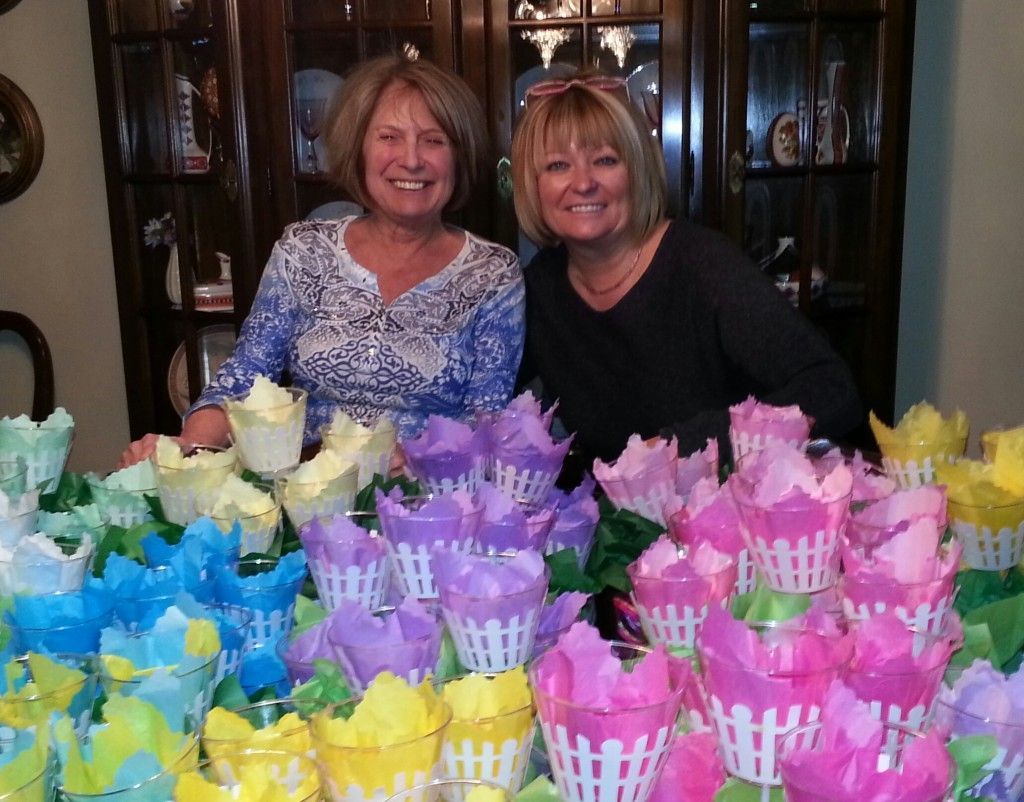 Two women standing in front of an array of fake flowers.