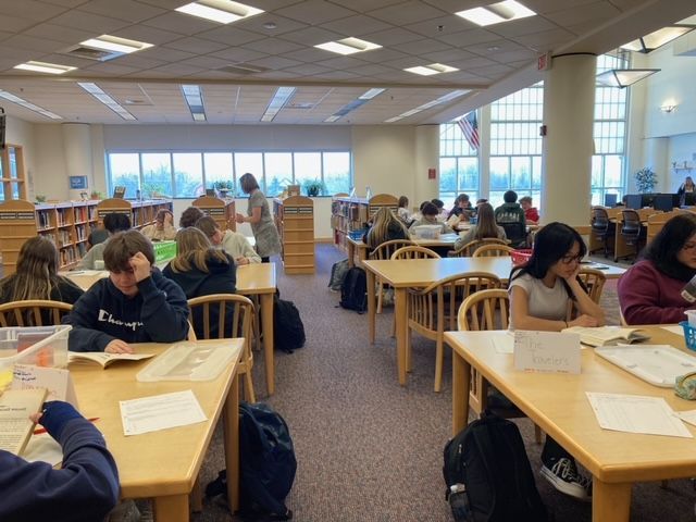 A group of students are sitting at tables in a library.