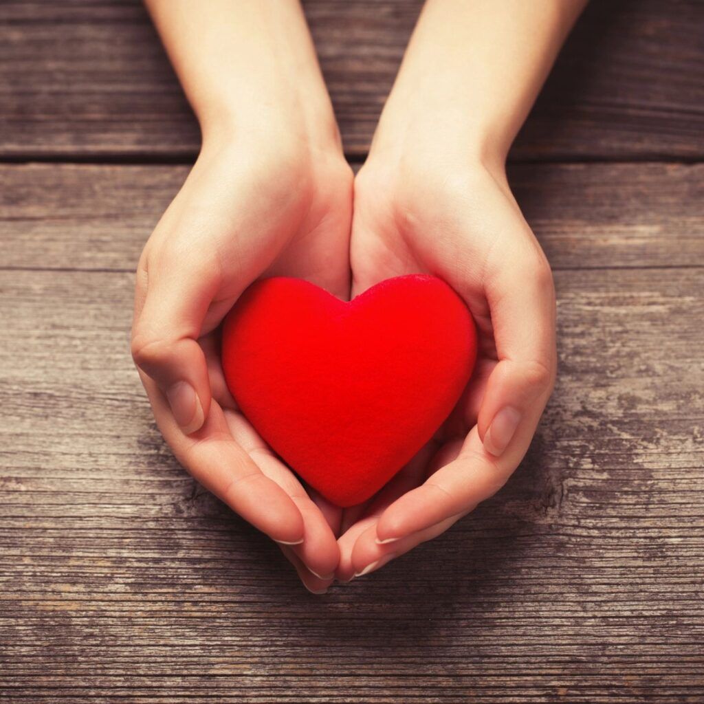 A person holding a red heart in their hands.