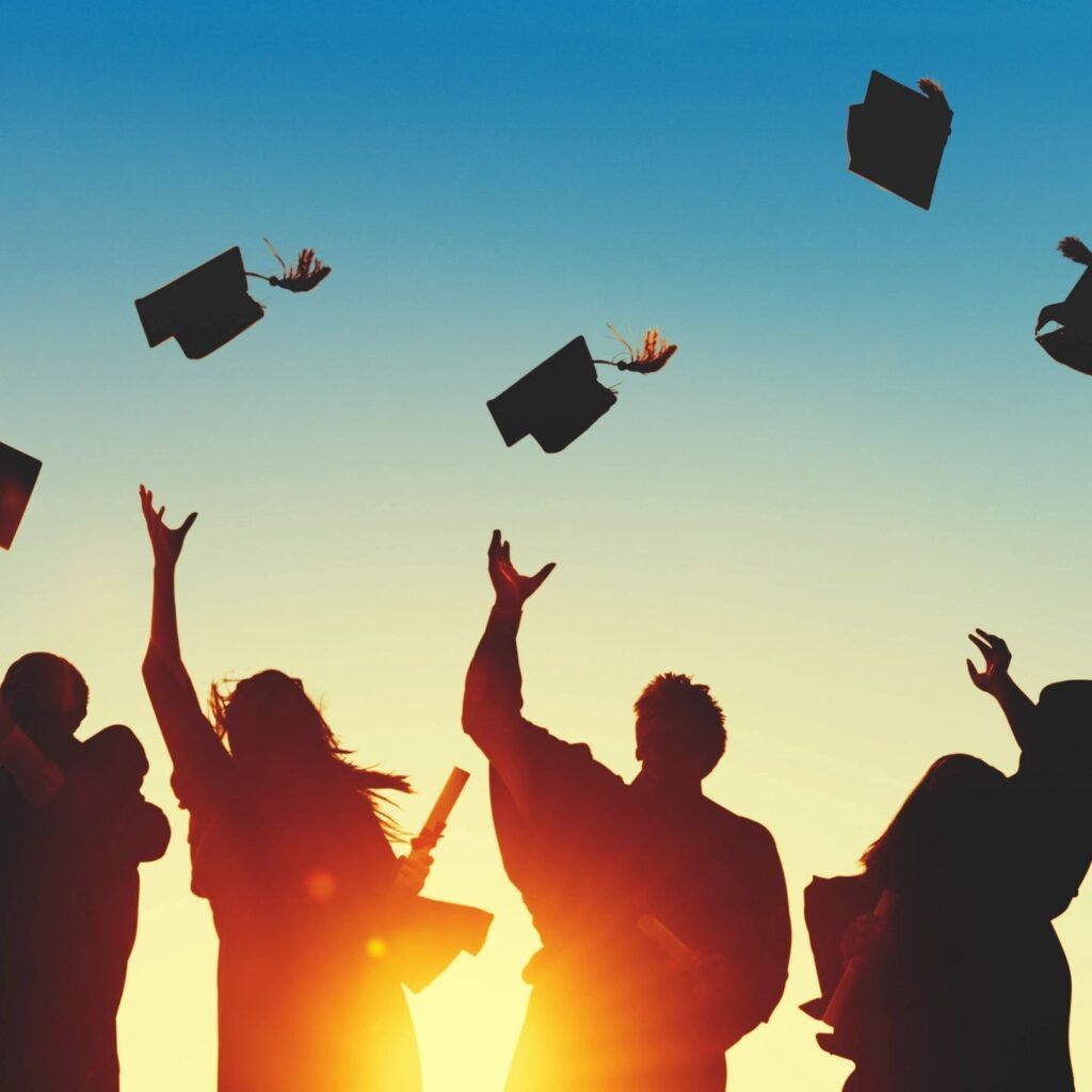 Teens throwing grad caps during sunset.