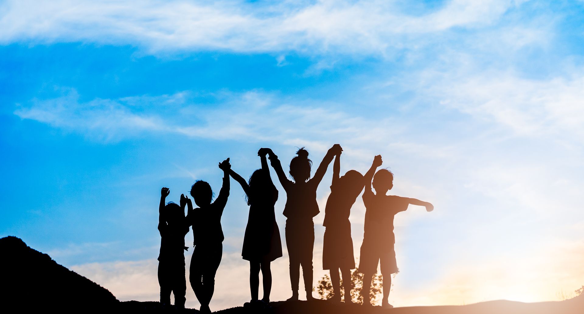 A group of children are standing on top of a hill holding hands.