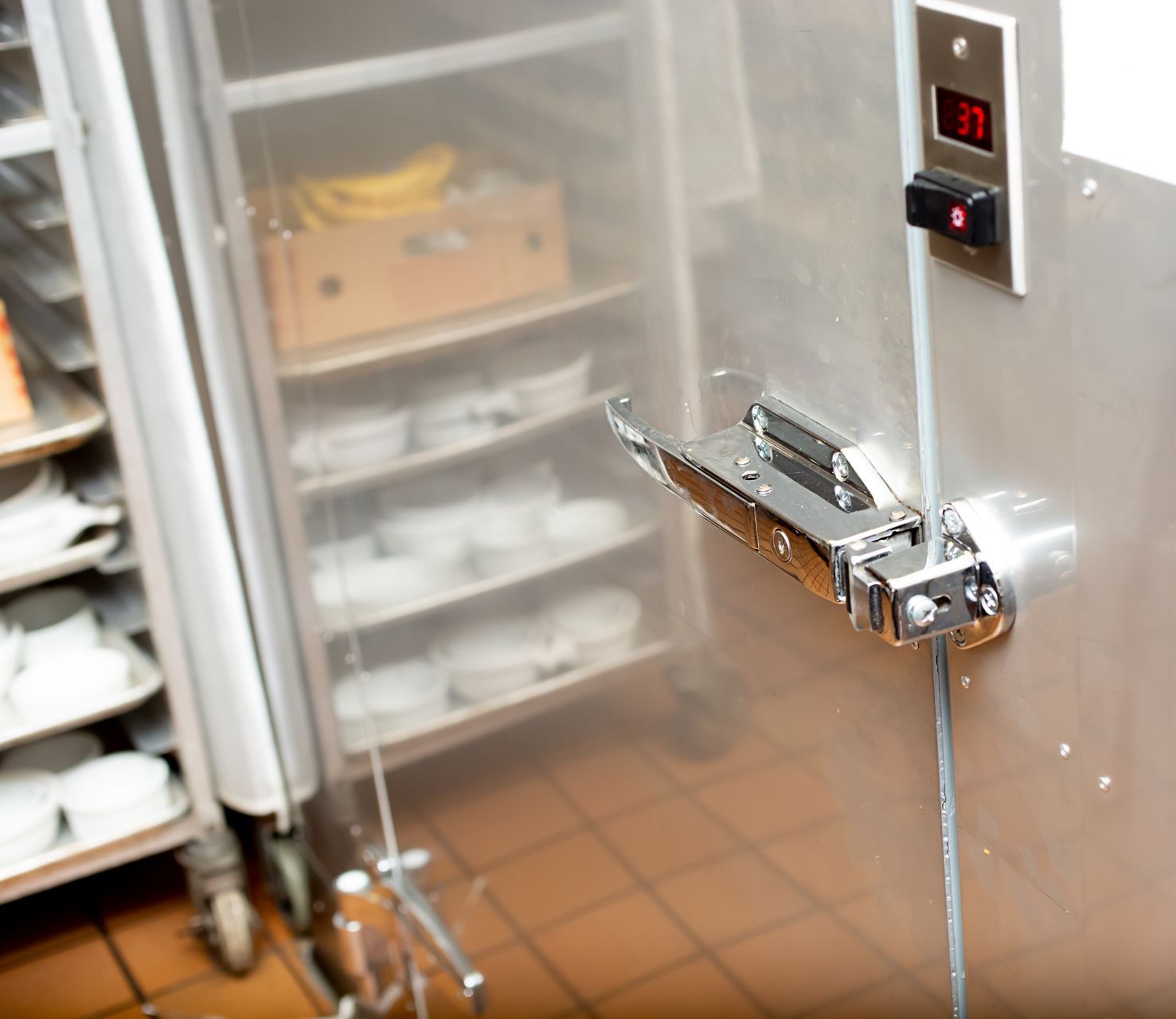 Close-up of a sturdy, silver door handle with a prominent grip, providing access to a walk-in fridge in a bustling restaurant kitchen.