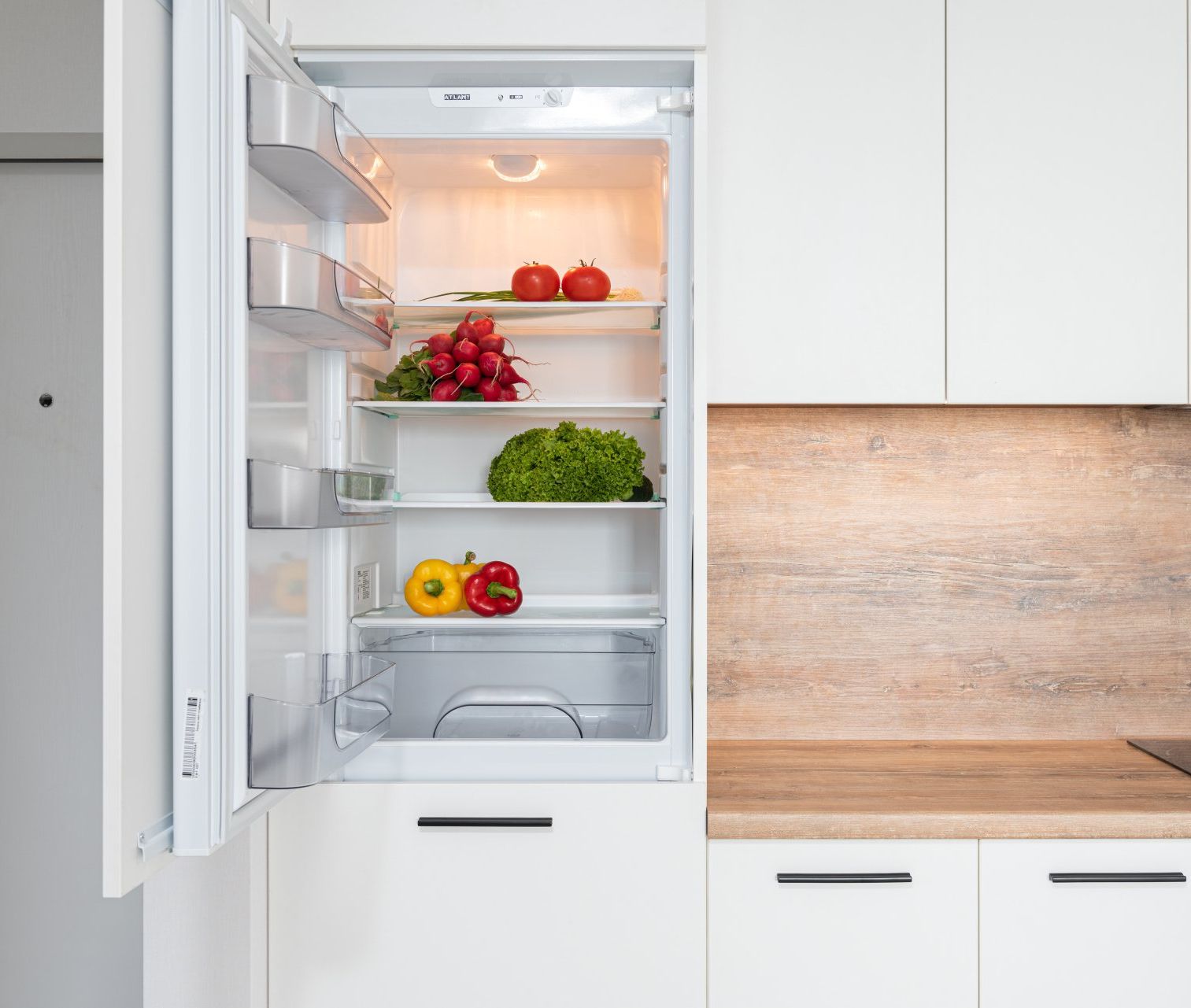 An open refrigerator revealing a vibrant assortment of fresh, colorful vegetables neatly arranged on its shelves.