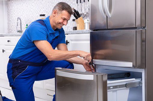A serviceman in uniform working on a refrigerator, carefully examining its inner components and making necessary repairs.