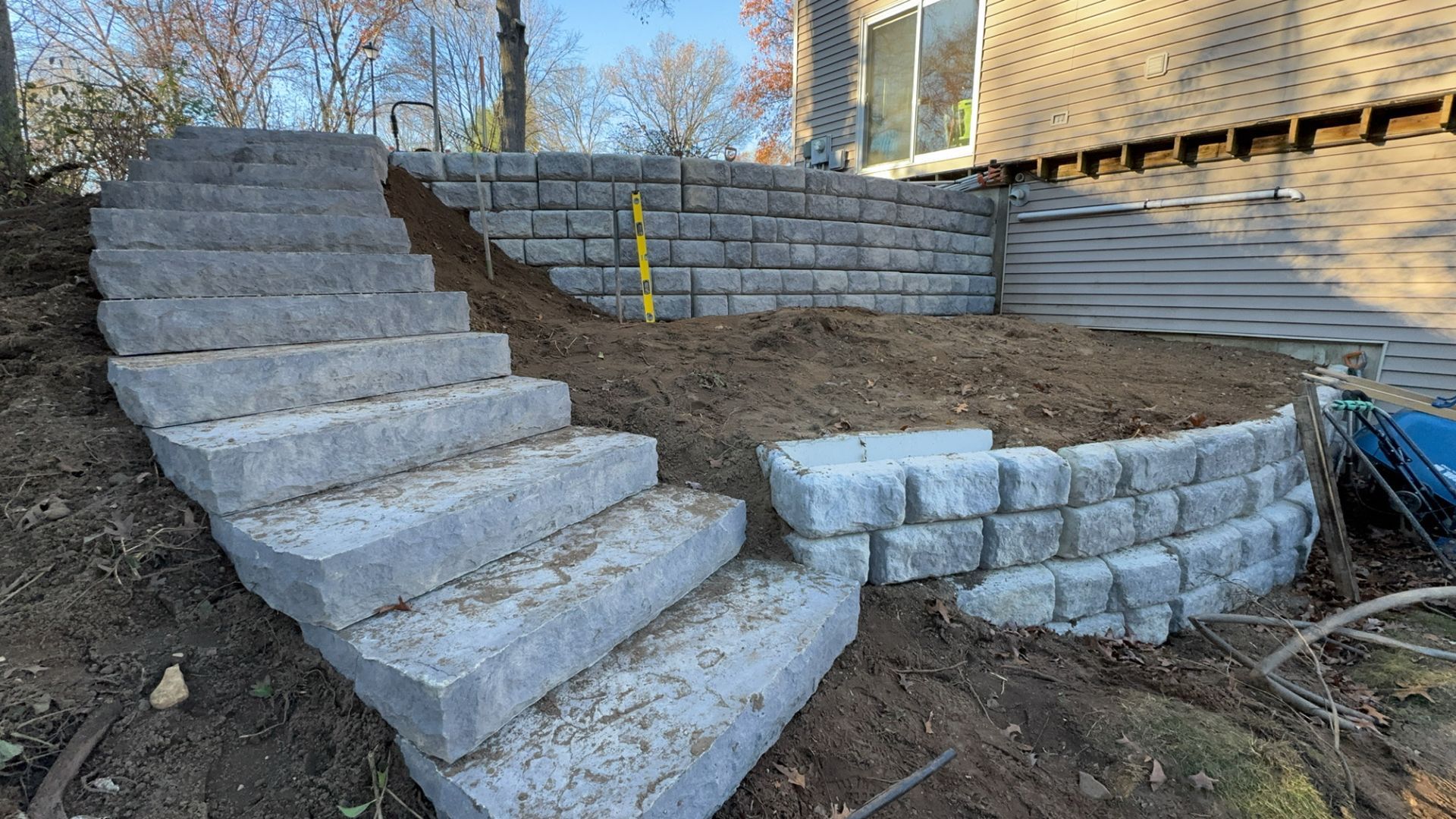 New gray stone steps and a curved retaining wall under construction in a residential backyard.