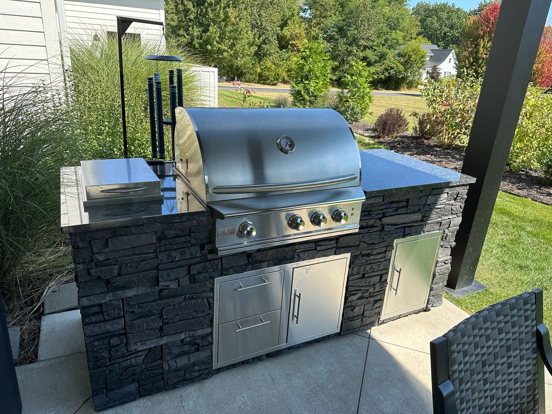 Outdoor kitchen island with a built-in stainless steel gas grill, storage doors, and dark stone masonry on a patio.