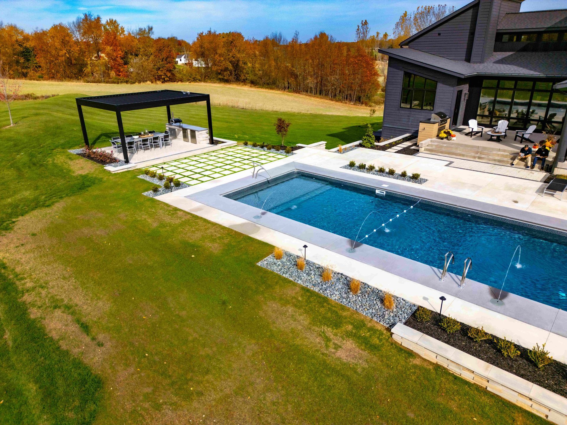 An aerial view of a backyard featuring a rectangular swimming pool, a patio area, and a covered pergola in autumn.