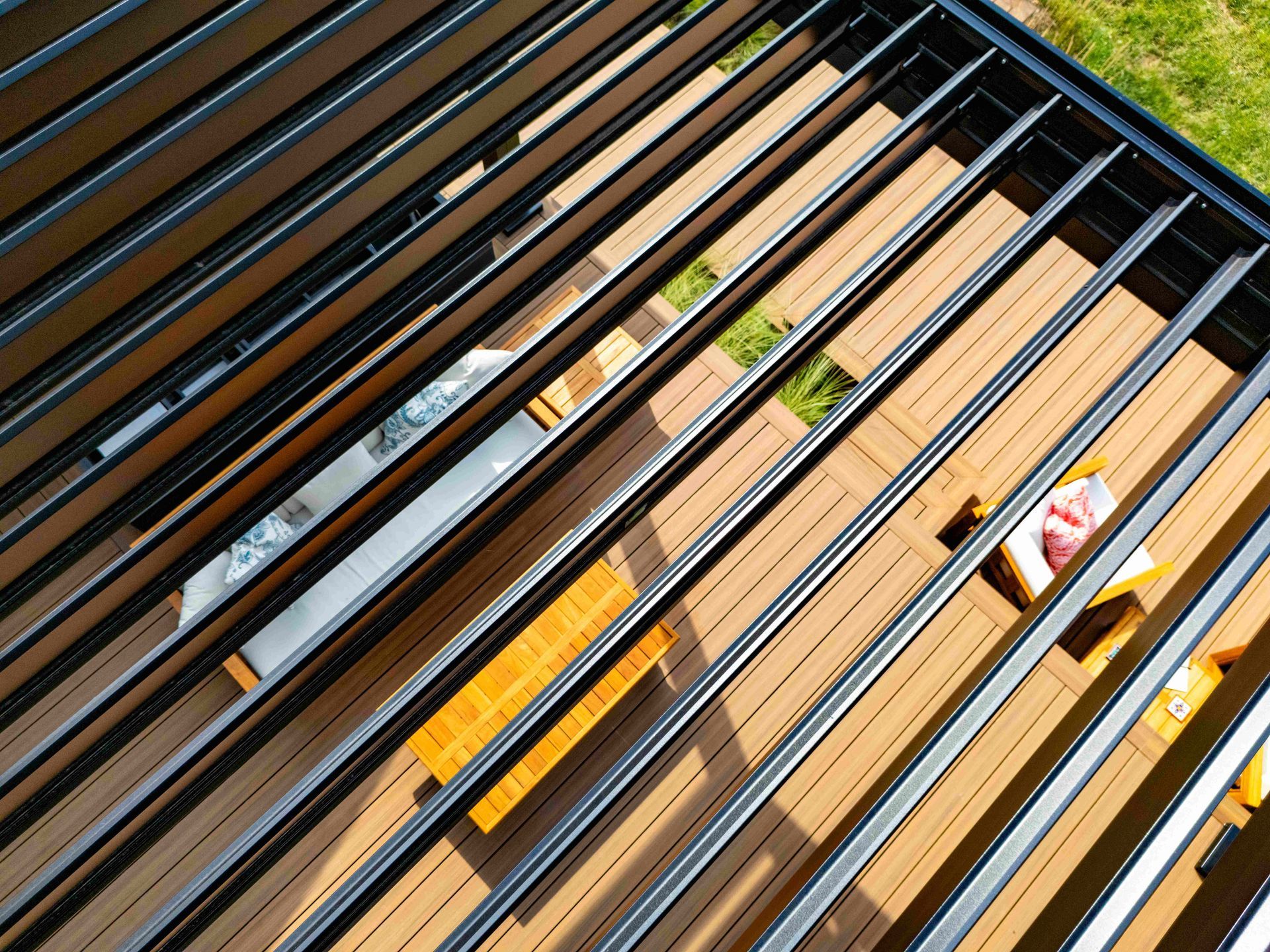 An aerial view looking through a black louvered pergola roof onto a wooden deck with outdoor seating.