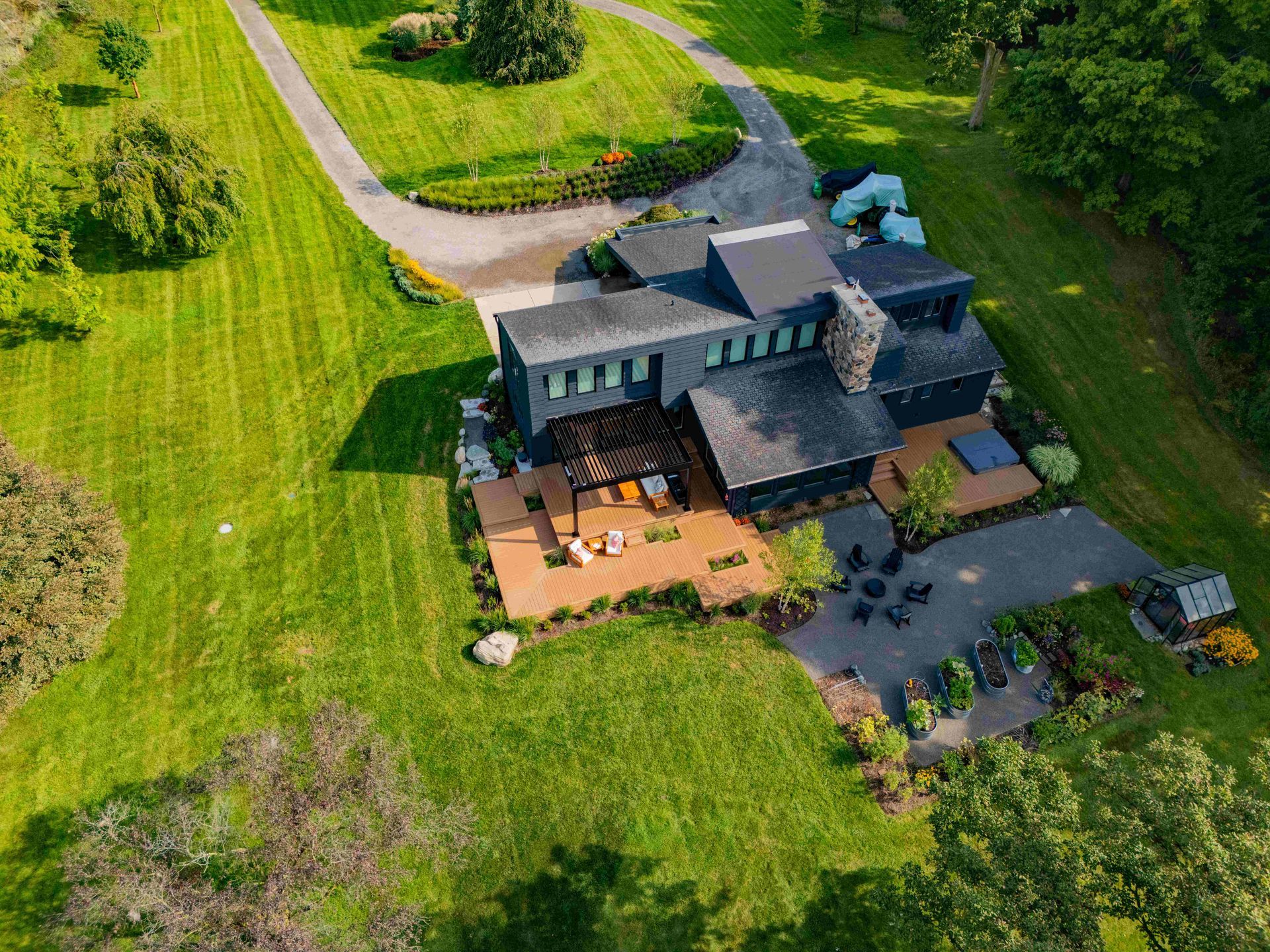 Aerial view of a modern dark-colored house with a wooden deck and surrounding lawn and trees.