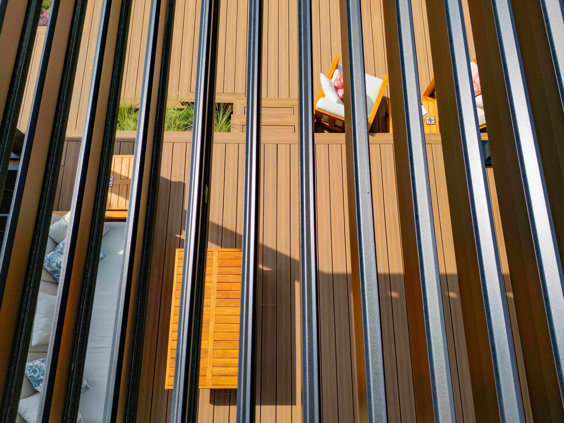 An elevated, downward view of a wooden deck with outdoor seating, partially obscured by a black louvered pergola roof.