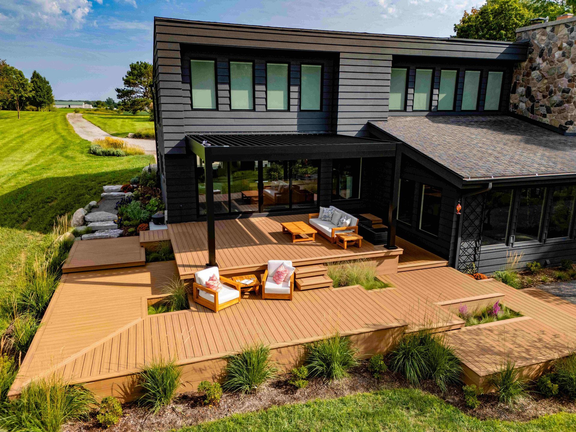 A modern, dark-sided home with a large, multi-level wooden deck featuring outdoor furniture and a covered patio area.