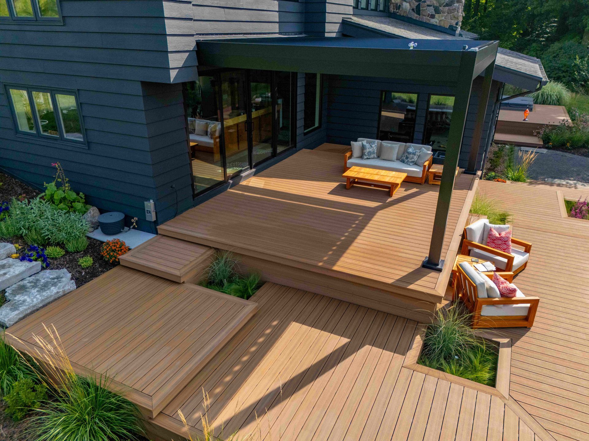 Multi-level wooden deck attached to a dark blue house, featuring a covered seating area and outdoor furniture.