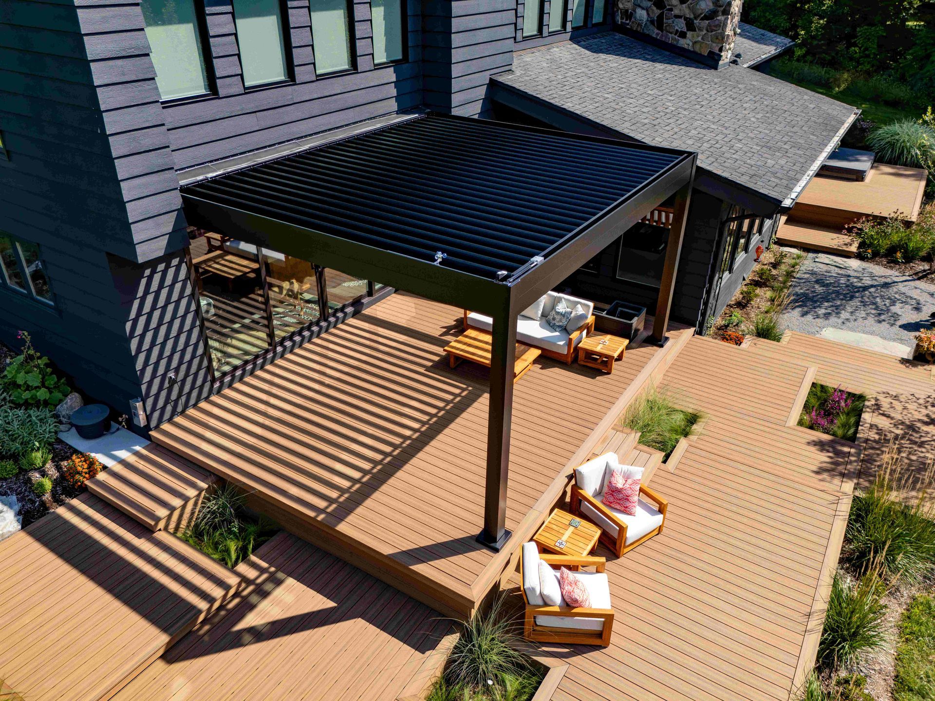 A high-angle view of a dark home patio with a black louvered pergola covering a deck area with outdoor furniture.
